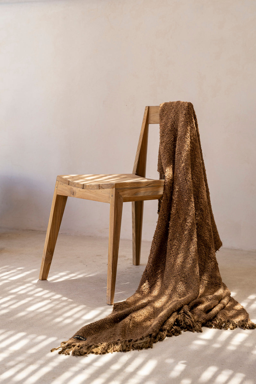 Chaise Paxi en teck dans un intérieur clair, avec un plaid posé sur le dossier