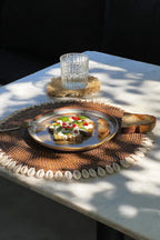 Table en marbre dressée avec un set de table en rotin et cauris, vue d'ensemble