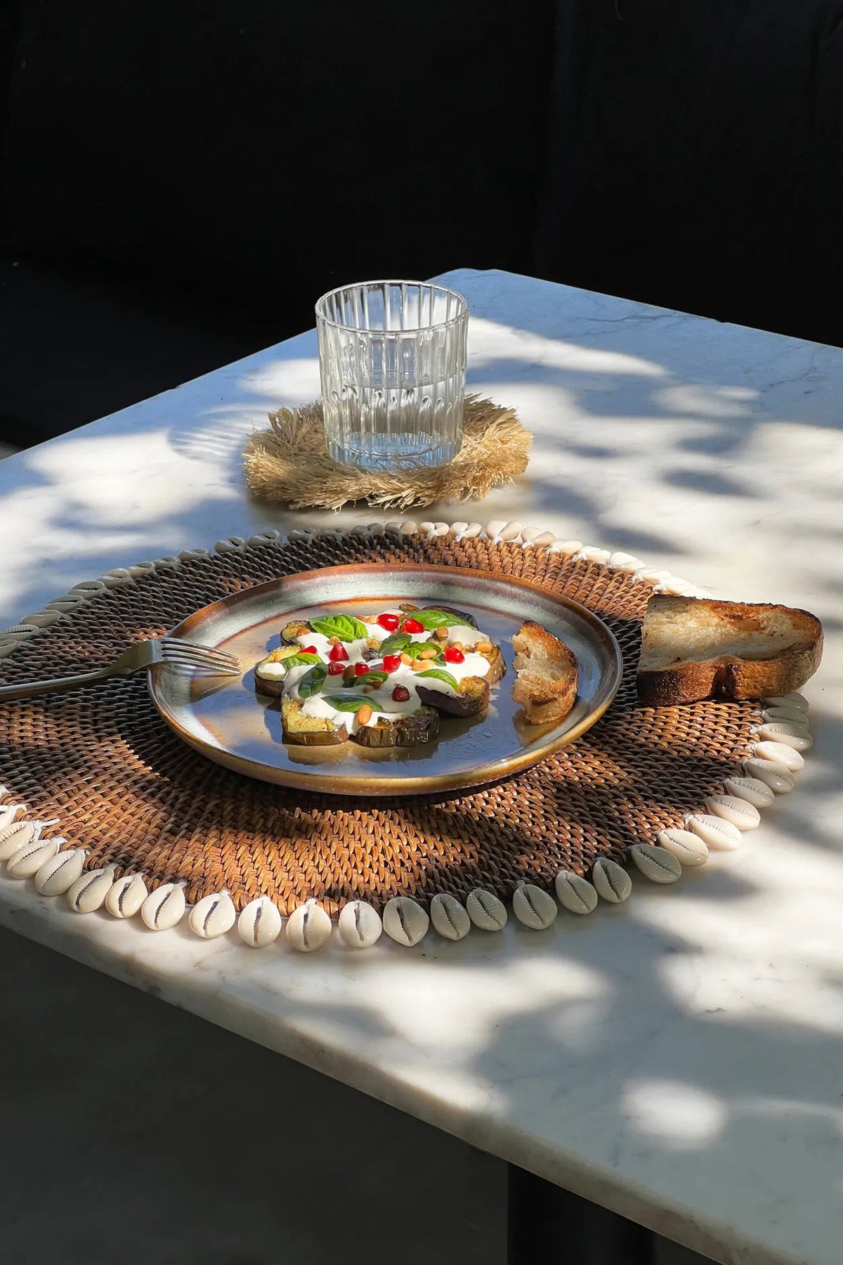 Table en marbre dressée avec un set de table en rotin et cauris, vue d'ensemble