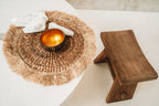Un set de table en jacinthe d'eau posé sur une table ronde claire, avec un bol doré et un tabouret en bois