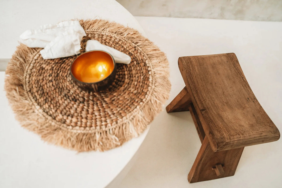 Un set de table en jacinthe d'eau posé sur une table ronde claire, avec un bol doré et un tabouret en bois