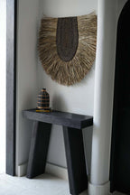 Décoration murale Nahla accrochée dans une entrée claire, au-dessus d'un tabouret sombre