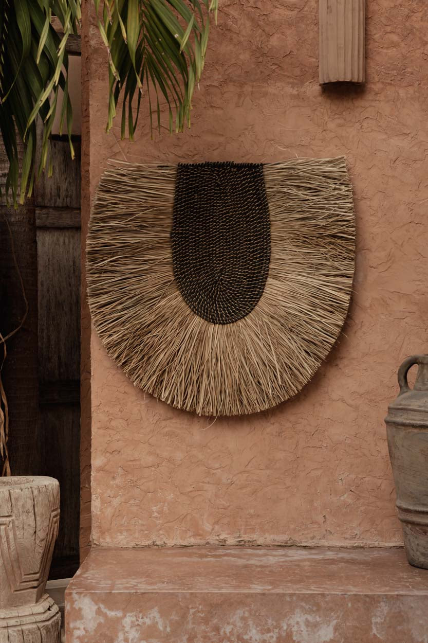 Décoration murale Nahla sur un mur terracotta, entourée de jarres en terre cuite