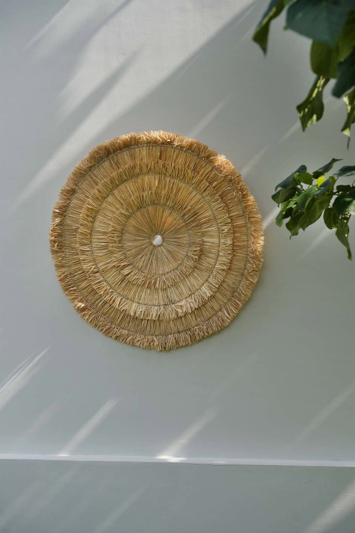 Décoration murale Sehseh accrochée sur un mur clair, feuillage à proximité