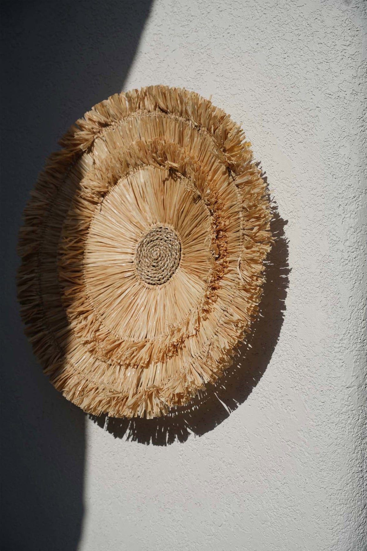 Décoration murale Wanita accrochée sur un mur clair, relief du tressage souligné par la lumière