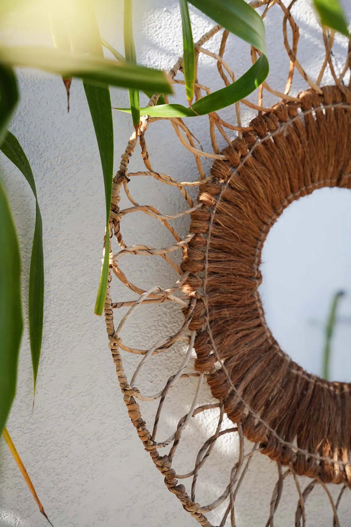 Miroir Montezuma accroché sur un mur clair, feuillage au premier plan