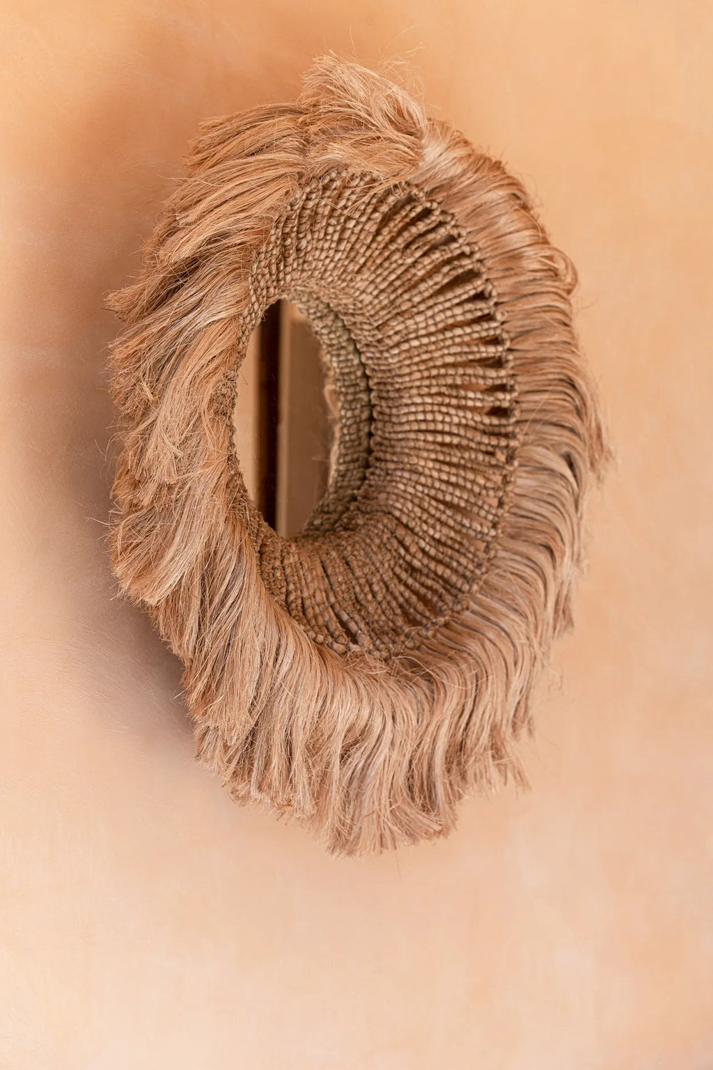 Miroir Salomon vu de biais sur un mur terracotta, relief de la frange souligné par la lumière