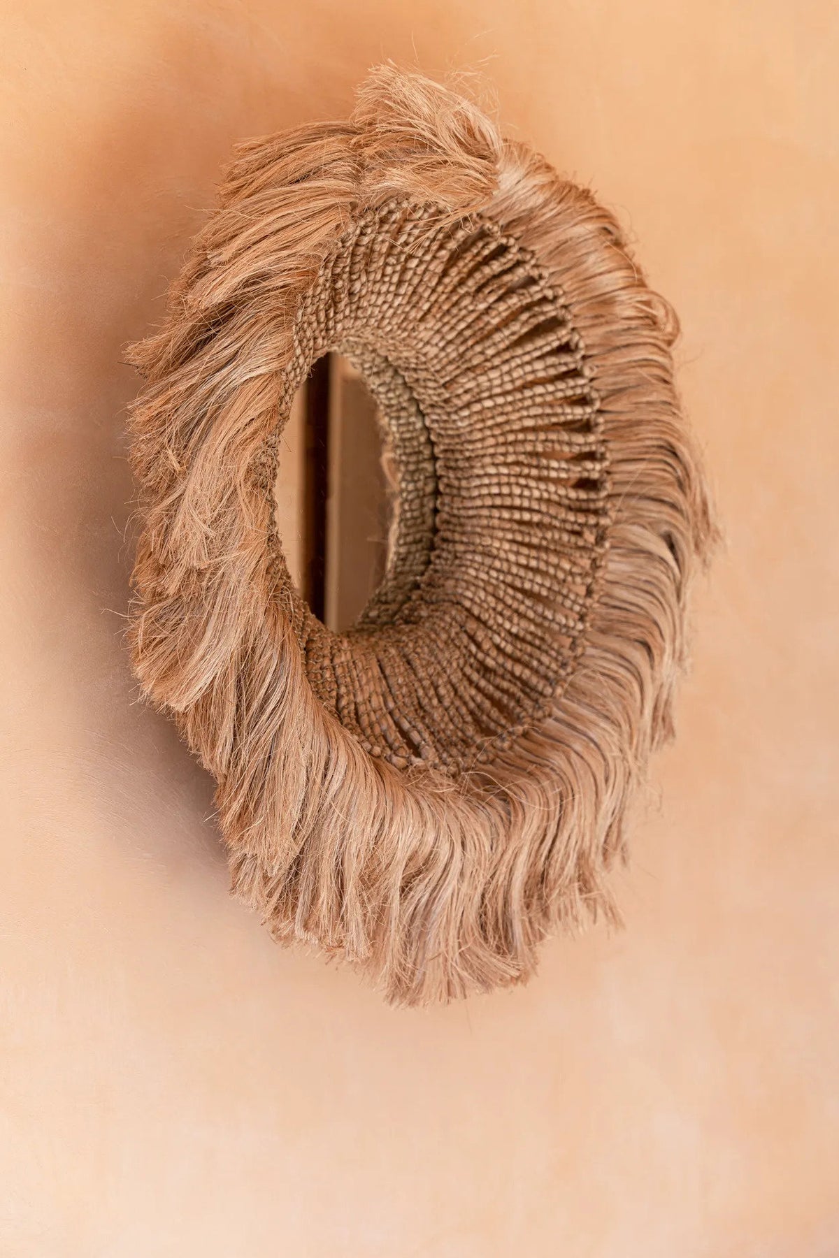 Miroir Salomon vu de biais sur un mur terracotta, relief de la frange souligné par la lumière