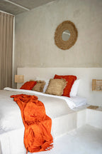 Miroir Yema dans une chambre aux murs clairs, linge de lit blanc et touches orangées