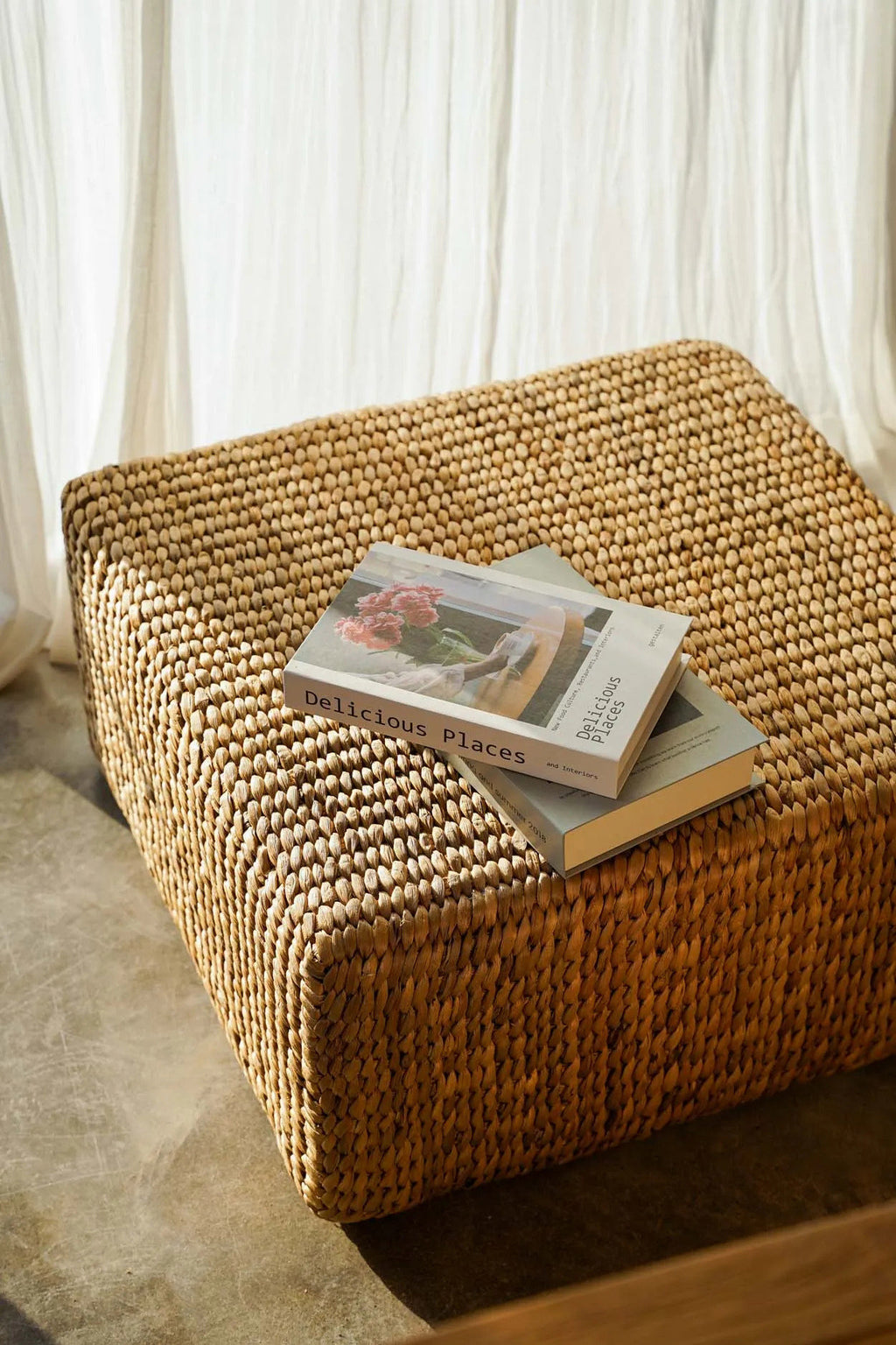 Pouf carré en jacinthe d'eau devant une banquette en teck, livres posés dessus